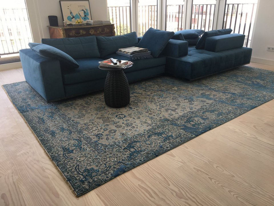 Gemusterter Teppich in Blautönen unter blauer Couch im Wohnzimmer